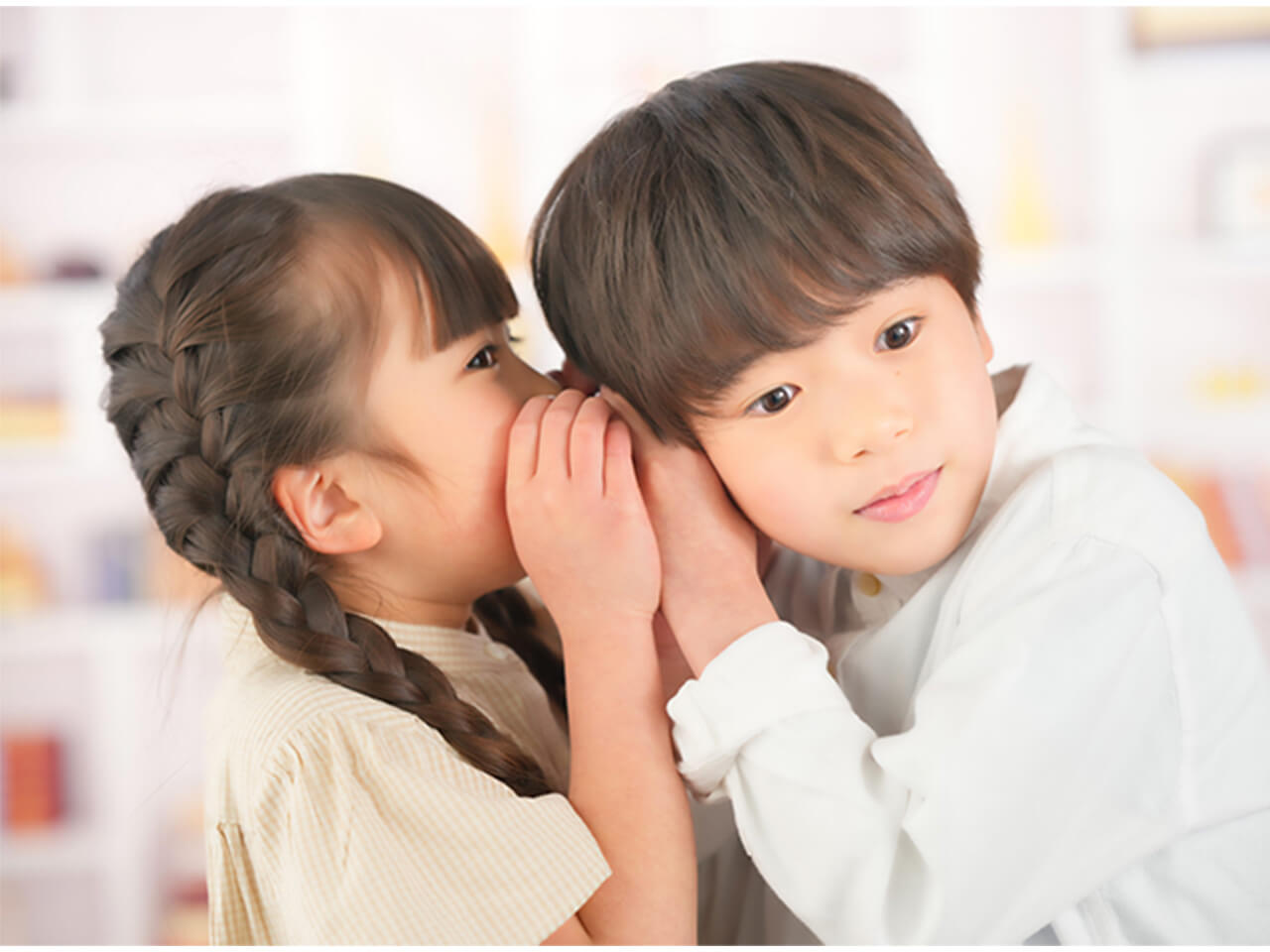 親しい様子の男女の子どもが耳元でささやき合っている写真。